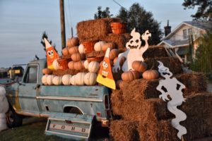 A truck bed is full of straw, with pumpkins and custom wooden candy corns and ghosts